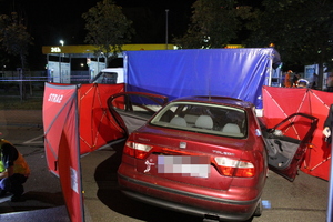 Zdjęcie przedstawia samochód m-ki Seat Toledo stojący przed czerwonym parawanem.