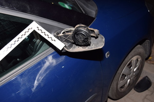 Zdjęcie przedstawia uszkodzone boczne prawe lusterko w samochodzie koloru granatowego. Obok niego znajduje się linijka technika.
