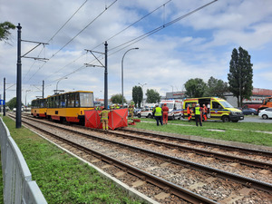Zdjęcie przedstawia miejsce wypadku. Widać stojący nieopodal tramwaj i namiot policyjny oraz policjantów, strażaków i pracowników tramwai, którzy są na miejscu.