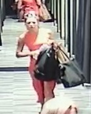 Zdjęcie przedstawia dwie kobietę w sklepie odzieżowym. Ma około 30 lat, około 170 cm wzrostu, szczupła budowa ciała, upięte blond włosy, ubrana w pomarańczową sukienkę, na ramieniu ma dwie czarne torebki. Po prawej stronie zdjęcia widać zasłony pomieszczenia przebieralni.