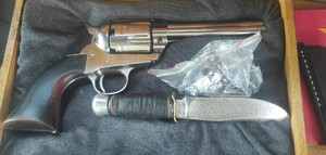 zdjęcie przedstawia broń palną w kolorze srebrnym z czarną rękojeścią, pod którą leży foliową torebka z zawartością foliowego zawiniątka. Pod nim leży nóż z czarną rękojeścią.