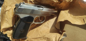 zdjęcie przedstawia broń w kolorze srebrnym z czarną rękojeścią leżącą na brązowym papierze.