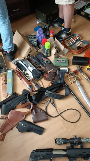 zdjęcie przedstawia leżące na podłodze opakowania z nabojami, pistolet pneumatyczny, noże, pokrowce na broń palną krótką.
