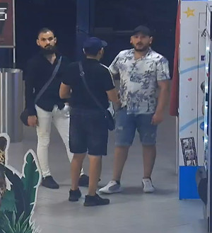 Zdjęcie przedstawia trzech mężczyzn o ciemniejszej karnacji, którzy stoją przed fotobudką. Dwaj z nich mają czarne czapki z daszkiem na głowach.