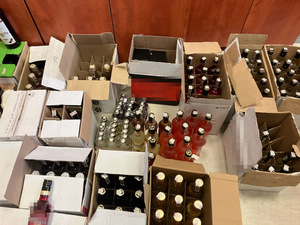 Zdjęcie przedstawia ustawione na podłodze kartony w kolorze białym i brązowym, w których znajdują się butelki z alkoholem.