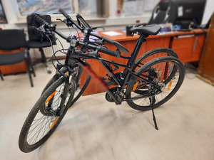 zdjęcie przedstawia dwa czarne rowery stojące w pomieszczeniu służbowym z jasną podłogą. Rowery są o sienie podparte, jeden z nich jest postawiony na nóżce.