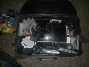 Zdjęcie przedstawia leżącą na asfalcie czarną walizkę z zawartością m.in. gier.