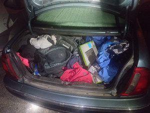 Zdjęcie przedstawia wnętrze bagażnika zabezpieczonego pojazdu. Znajdują się tam plecak, odzież i klawiatura od karton na którym widnieje zdjęcie klawiatury komputera.
