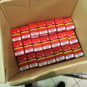 Zdjęcie przedstawia czerwone paczki od papierosów zapakowane w kartonowe otwarte pudło.