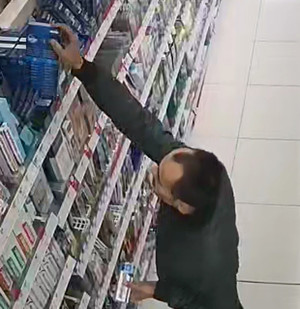 Zdjęcie przedstawia mężczyznę sięgającego do półki z asortymentem. Mężczyzna ma około 35 lat, około 185 cm wzrostu, jest szczupłej budowy ciała, ma ciemne włosy z zakolami.