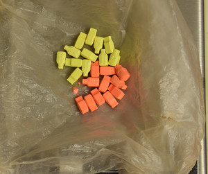Zdjęcie przedstawia leżące na foliowej torebce tabletki w kolorze żółtym i pomarańczowym.