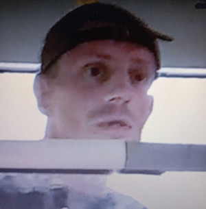 Zdjęcie przedstawia mężczyznę wewnątrz autobusu. Jest on w wieku około 40, na głowie ma czarną czapkę z daszkiem.