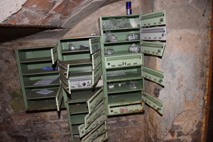 Zdjęcie przedstawia zielone skrzynki pocztowe z otwartymi drzwiami, w których znajdują się foliowe torebeczki ze srebrnymi zawiniątkami.