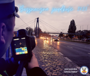 Zdjęcie przedstawia policjanta patrzącego na ekran radaru mierzącego prędkość pojazdów poruszających się drogą.
