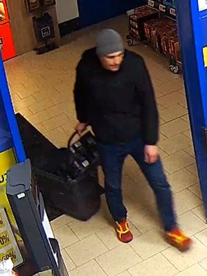 Zdjęcie przedstawia mężczyznę wchodzącego do sklepu. Jest on w wieku około 35 lat, ma około 190 cm wzrostu, przeciętną budowę ciała; ubrany jest w ciemnoniebieską kurtkę, niebieskie jeansy, sportowe czerwone buty z żółtymi obszyciami, szarą czapkę materiałową. W lewej dłoni trzyma plastikowy koszyk sklepowy.