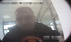 Zdjęcie przedstawia fragment sylwetki mężczyzny wypłacającego pieniądze z bankomatu. Mężczyzna jest skierowany wprost do kamery znajdującej się w bankomacie.