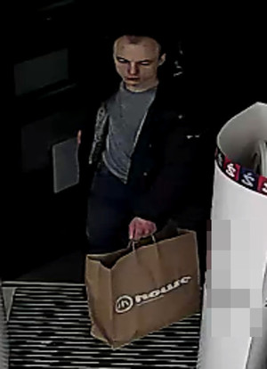 Zdjęcie przedstawia mężczyznę w wieku około 25 lat, około 175 cm wzrostu, szczupłej budowy ciała, z ciemnymi włosami i widocznymi zakolami na czole; ubrany jest w czarną kurtkę, szarą koszulkę, spodnie jeansowe, buty sportowe w kolorze czarnym. W lewej dłoni trzyma dużą brązową papierową torbę na zakupy z logo firmy &amp;quot;House&amp;quot;. Jest skierowany przodem do obiektywu kamery.