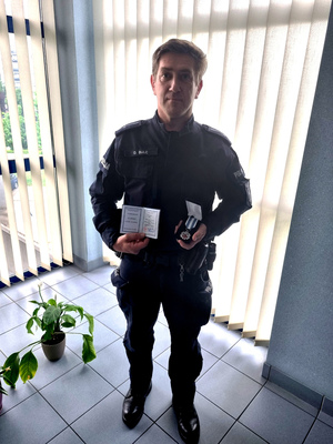 Zdjęcie przedstawia umundurowanego policjanta, który stoi przodem do obiektywu aparatu. Trzyma w dłoniach pudełko z odznaką.