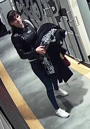 Zdjęcie przedstawia kobietę w sklepie - wiek około 28 lat, czarne związane włosy, prosta grzywka; ubrana jest w czarną skórzaną kurtkę, białą koszulkę, niebieskie spodnie jeansowe oraz białe sportowe buty, na ramieniu nosi jasną torbę.
Stoi przodem do kamery monitoringu.