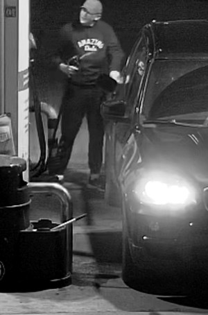 Zdjęcie przedstawia mężczyznę stojącego pomiędzy samochodem, a dystrybutorem. Mężczyzna trzyma w prawej ręce przewód do nalewania paliwa. Ma około 50 lat, około 180 cm wzrostu, tęgą budowę ciała. Ubrany jest w jasną czapkę z daszkiem typu bejsbolówka, ciemną bluzę i ciemne spodnie oraz buty.