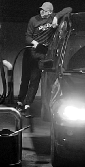 Zdjęcie przedstawia mężczyznę stojącego pomiędzy samochodem, a dystrybutorem. Mężczyzna trzyma w prawej ręce przewód do nalewania paliwa. Lewą opiera się na dachu samochodu. Ma około 50 lat, około 180 cm wzrostu, tęgą budowę ciała. Ubrany jest w jasną czapkę z daszkiem typu bejsbolówka, ciemną bluzę i ciemne spodnie oraz buty.