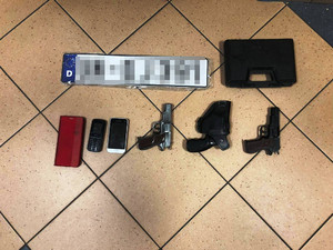 Zdjęcie przedstawia przedmioty rozłożone na podłodze, w tym telefony i broń.