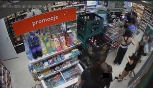 Zdjęcie przedstawia wnętrze sklepu, a w nim kobietę o długich ciemnych włosach, której twarz jest zasłonięta czarnym prostokątem. Niedaleko niej wdać kilka młodych osób, których twarz są zasłonięte komputerowym filtrem.