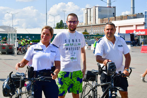Zdjęcie przedstawia trzech stojących mężczyzn. dwóch z nich trzyma przed sobą rowery. Wszyscy uśmiechają się do zdjęcia.
