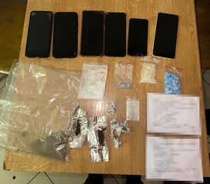 Zdjęcie przedstawia czarne telefony komórkowe i foliowe zawiniątka i torebeczki z różną zawartością leżące na stole.