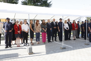 Zdjęcie przedstawia uczestników uroczystości stojących pod białym zadaszeniem.