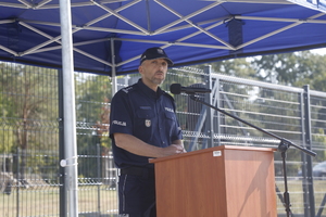 Zdjęcie przedstawia umundurowanego policjanta stojącego przed mikrofonem.