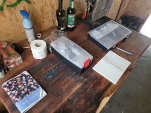 Zdjęcie przedstawia różne przedmioty ułożone na stole, w tym plastikowy przezroczysty pojemnik, zeszyt.
