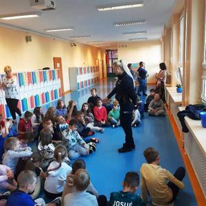 Zdjęcie przedstawia umundurowaną policjantkę, która stoi przed dziećmi siedzącymi na dywanie.