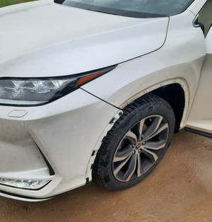 Zdjęcie przedstawia fragment białego pojazdu. Pojazd ma widoczne uszkodzenie przedniego lewego nadkola.