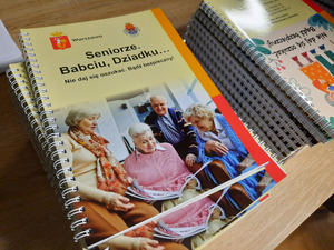 Zdjęcie przedstawia broszury informacyjne pod tytułem: &quot;Seniorze. Babciu, Dziadku... Nie daj się oszukać! Bądź bezpieczny&quot; ułożone w stosie na stole.