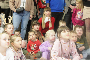 Zdjęcie przedstawi dzieci siedzące na podłodze, które wpatrują się przed siebie z uśmiechem na twarzy.