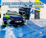 Zdjęcie przedstawia oznakowany radiowóz zaparkowany na tle wysokiego budynku.