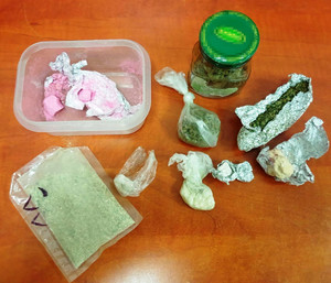 Zdjęcie przedstawia leżące na stole pojemniki, zawiniątka z suszem roślinnym oraz słoik z zieloną zakrętką.