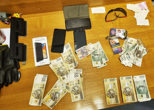 Zdjęcie przedstawia leżące na stole przedmioty, pieniądze  w różnych nominałach oraz telefony komórkowe.