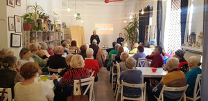 Zdjęcie przedstawia dwie policjantki stojące przed siedzącymi na krzesłach seniorami.