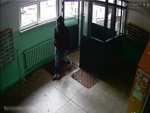 Zdjęcie przedstawia ubranego na ciemno mężczyznę, który wchodzi na korytarz bloku.