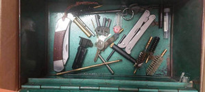 Zdjęcie przedstawia różne przedmioty w tym dwa noże zapakowane w metalowe pudełko.