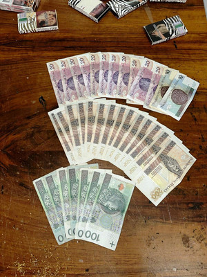Zdjęcie przedstawia banknoty ułożone na stole, w górze zdjęcia widać kilka paczek papierosów.