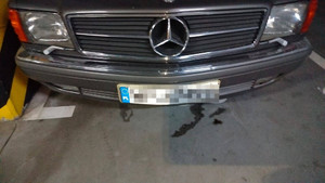 Zdjęcie przedstawia fragment przodu pojazdu m-ki BMW, który ma zasłoniętą tablicę rejestracyjną.