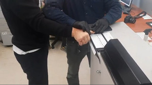 Zdjęcie przedstawia nieumundurowanego policjanta, który pobiera odciski palców zatrzymanemu mężczyźnie.