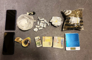 Zdjęcie przedstawia telefony, pieniądze i zawiniątka z różnymi substancjami rozłożone na ciemnym blacie stołu.