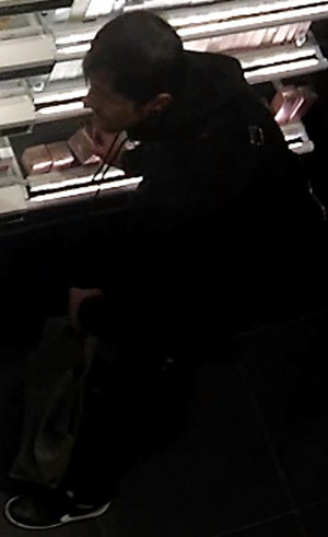 Zdjęcie przedstawia fragment sylwetki mężczyzny ubranego na ciemno, który kuca przed półką z kosmetykami.