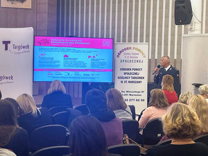 Zdjęcie przedstawia policjanta stojącego przed ludźmi siedzącymi na widowni.