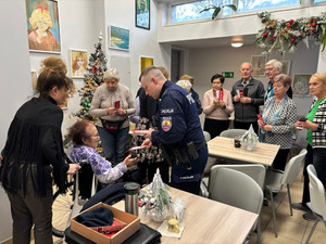 Zdjęcie przedstawia policjanta, który wręcza seniorom ulotki profilaktyczne.