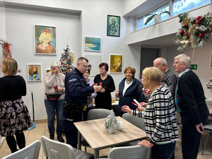 Zdjęcie przedstawia policjanta, który wręcza seniorom ulotki profilaktyczne.